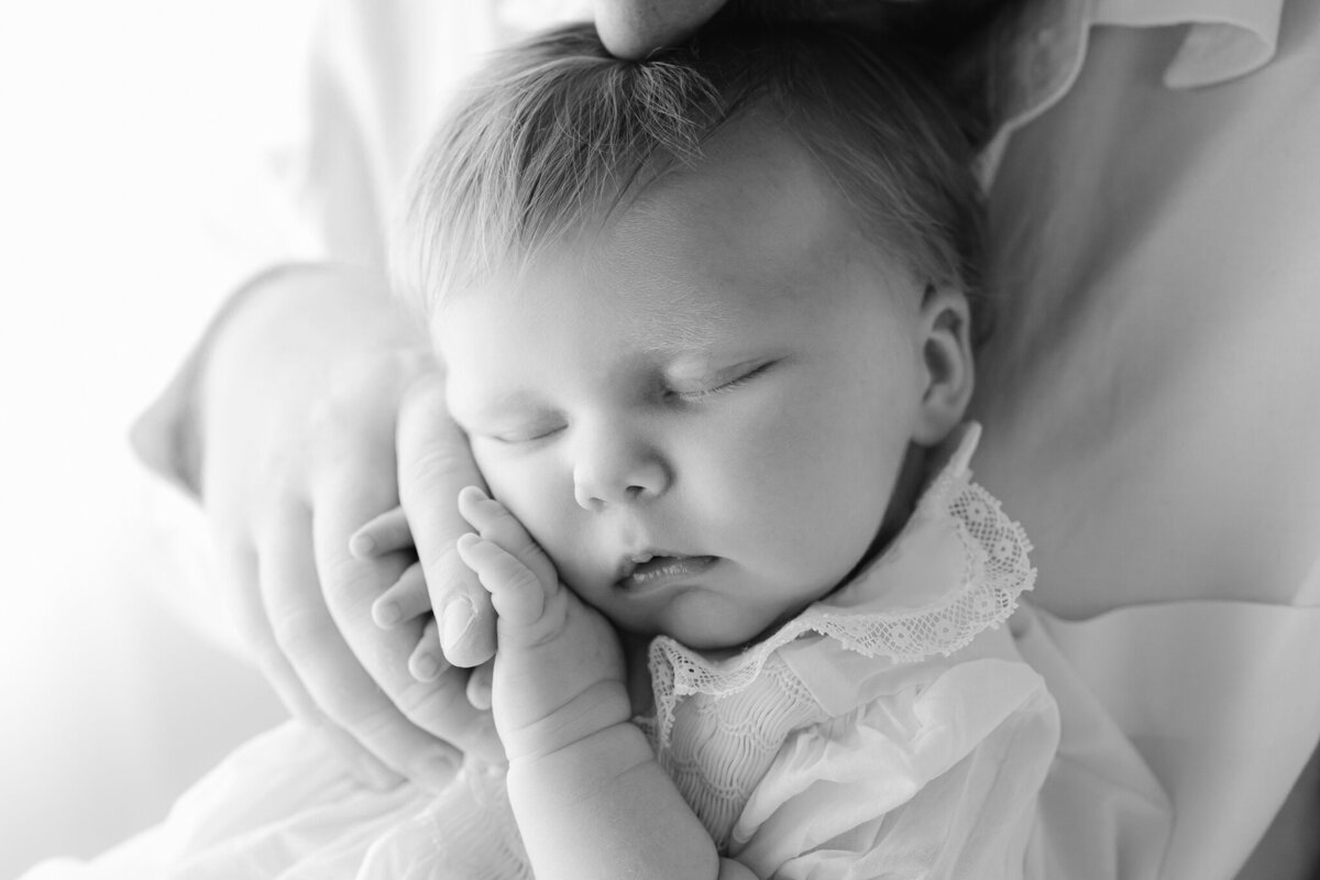 black and white image of a newborn baby girl holding her fathers fingers.