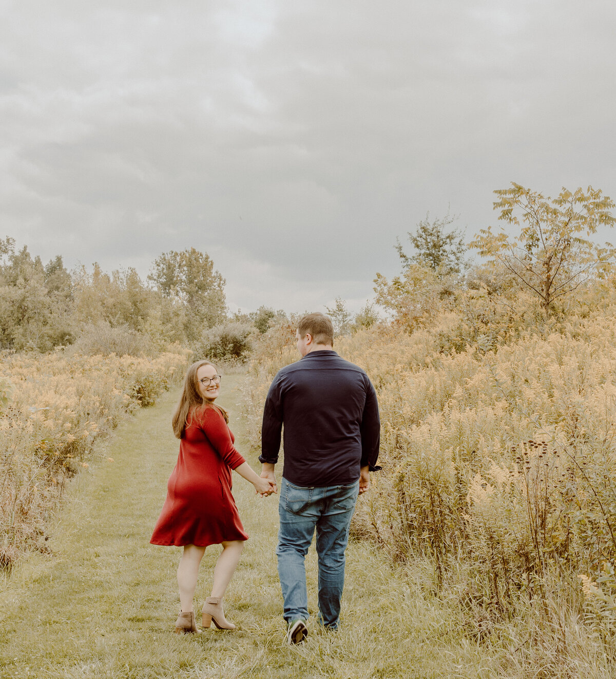 couple holding hands in field during engagement session