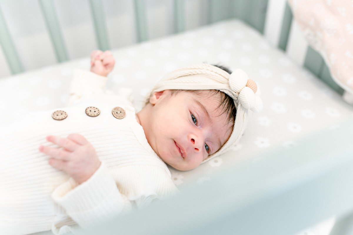 Newborn resting peacefully in a soft, neutral-toned nursery – captured by a Birmingham newborn photographer. A sweet baby girl gazes gently from her crib, wrapped in cozy textures with delicate details, reflecting a warm and serene lifestyle newborn session.