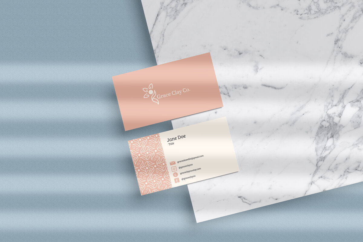 Grace Clay Co business cards created by Ayanna Richilano Designs sitting on a white with black marble with a dusty blue background.