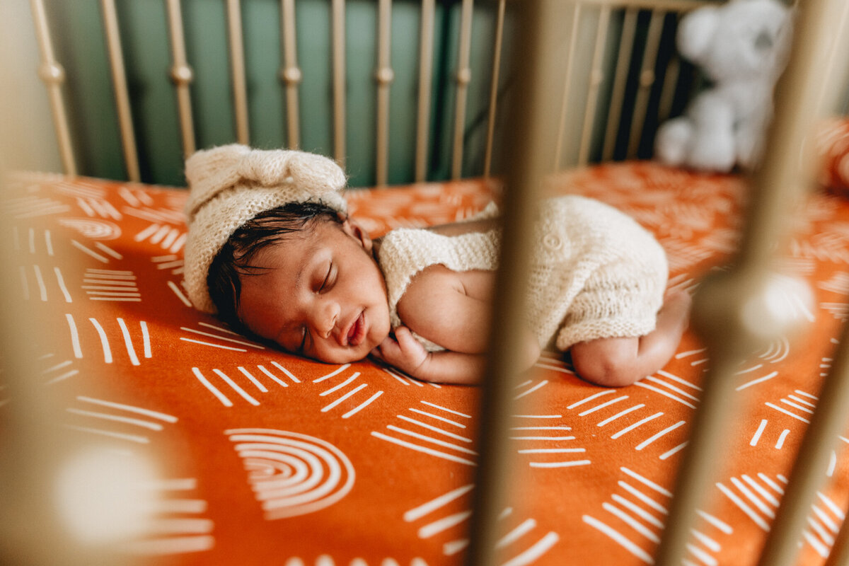 Infant photographer capturing newborn baby sleeping in a crib.
