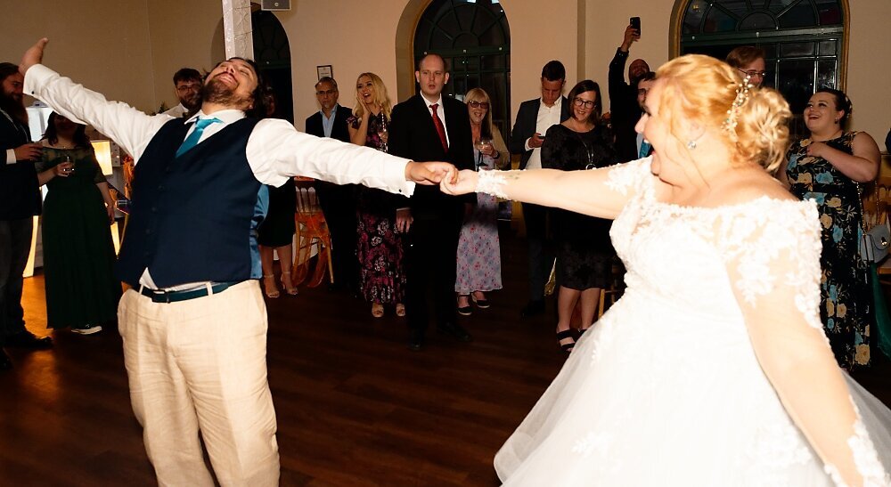 First dance of a bride and groom laughing and holding hands with wedding guests in background