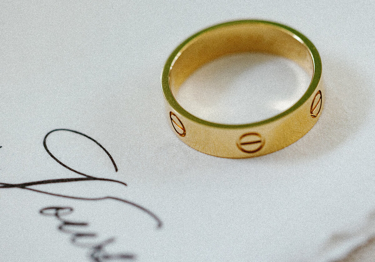 A close-up of a gold Cartier wedding band placed elegantly on a vow card, showcasing intricate wedding details, captured by Claudia Amalia Photography.