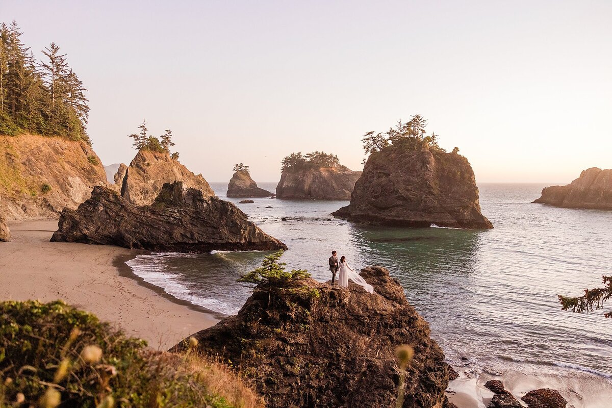 A bride and groom stand on a cliff edge at Secret Beach in Oregon.
