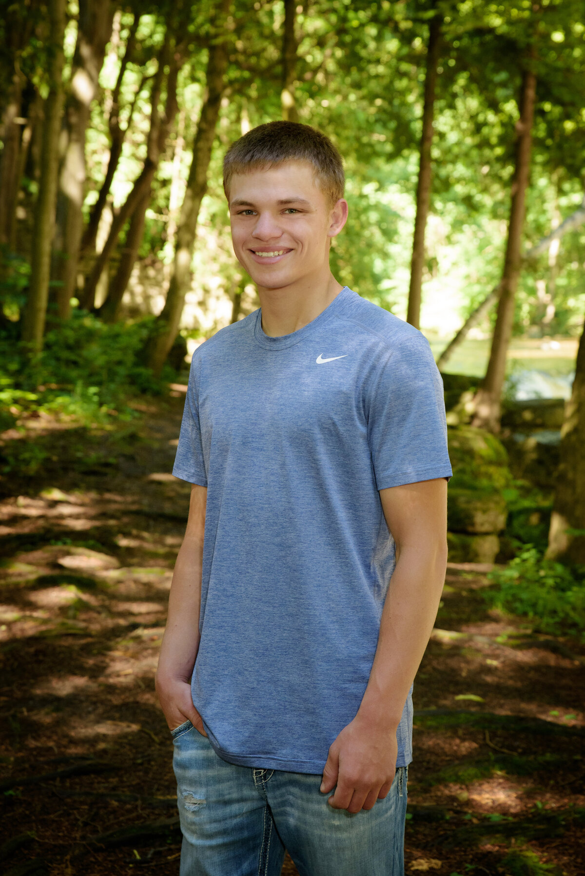 Luxemburg Casco high school senior boy wearing a short sleeve blue t-shirt and jeans sitting standing on walking path in the woods at Devil's River Campground near Green Bay, Wisconsin.