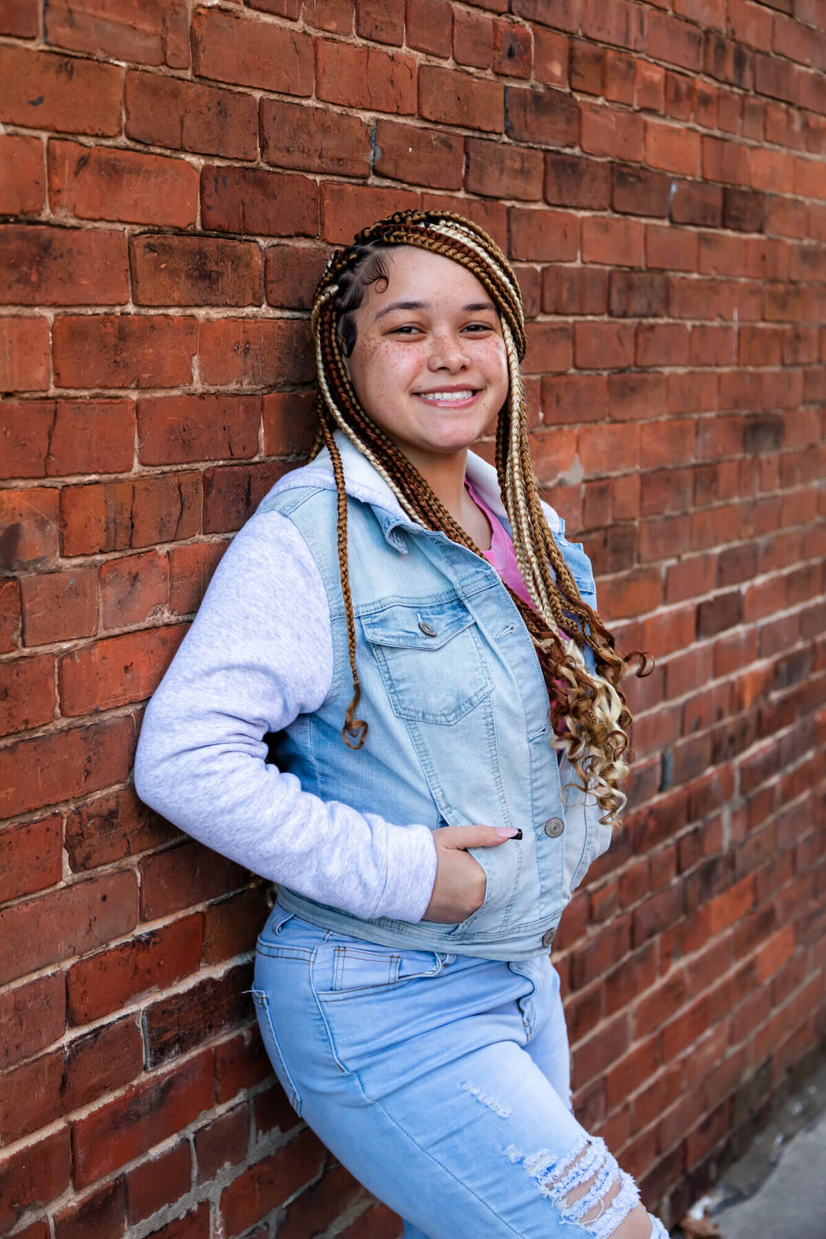Beautiful high school senior girl with braids wearing a denim hoodie and leaning on a brick wall. Captured by Springfield, MO senior photographer Dynae Levingston.
