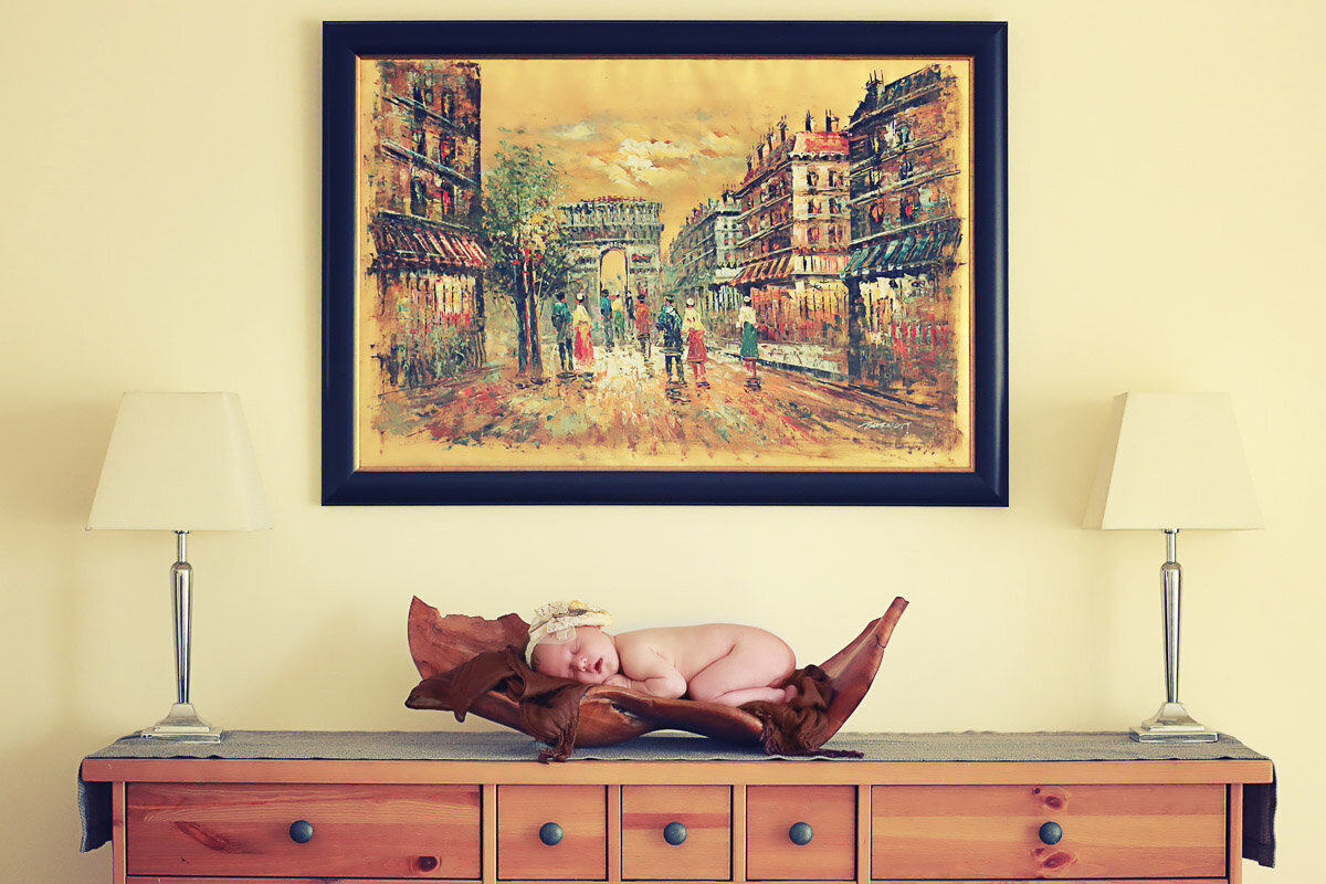 Newborn baby sleeping on her tummy in wooden crate on the drawer under the classic picture at home in Bearspaw Alberta
