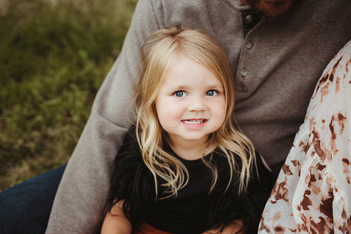 A detailed shot of a daughter sitting on her dad's lap is looking up at the camera.