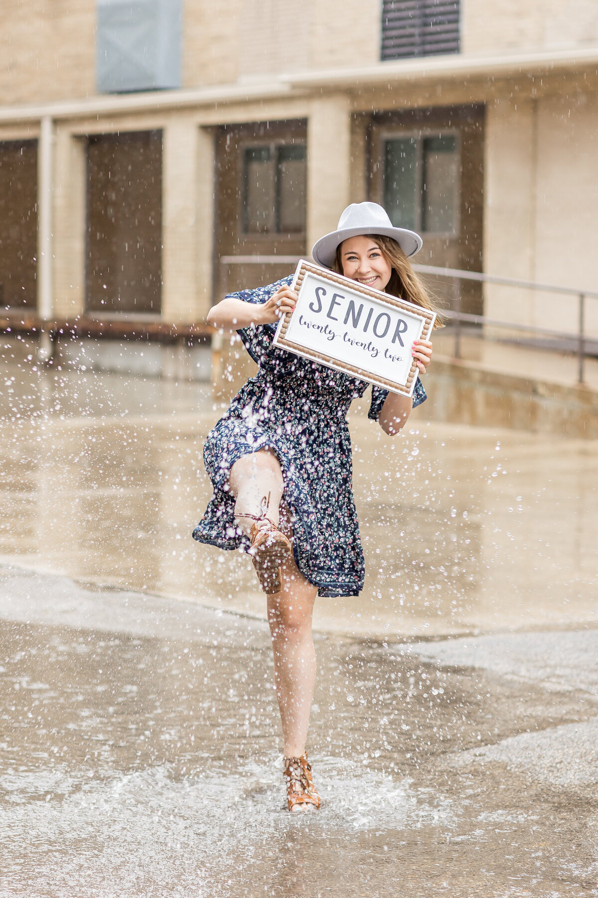 a girl holding a sign with her graduation  year and kicking water in the rain