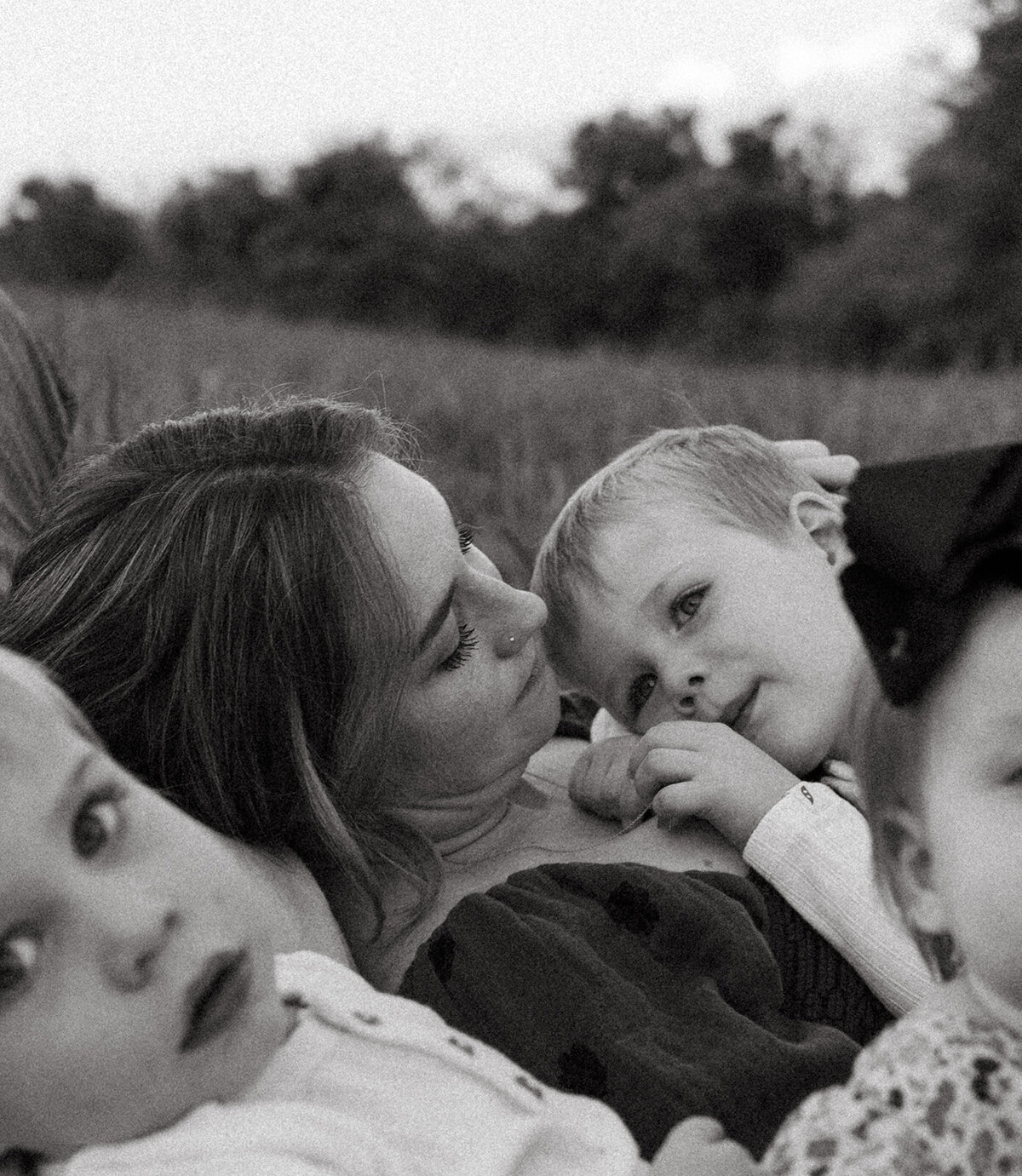 Mother lying in a grassy field with her toddler son cuddled on top during a candid outdoor motherhood session