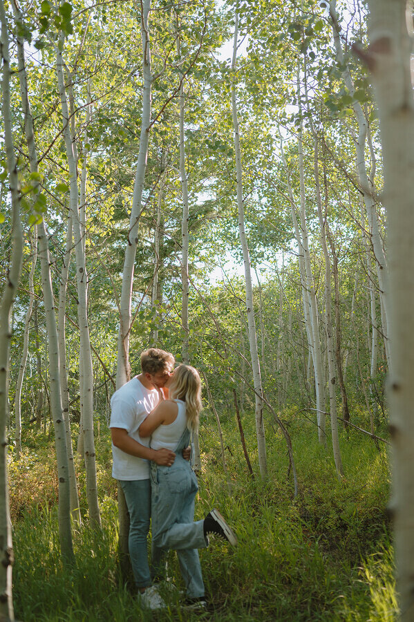 A man and woman kiss in a grove of birch trees. The photo tells the story of their romance.