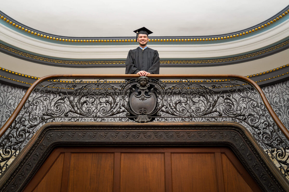 college graduation photography of a college senior in his cap and gown atop a symmetrical staircase. Captured at William Pitt Union, University of Pittsburgh, Pittsburgh PA