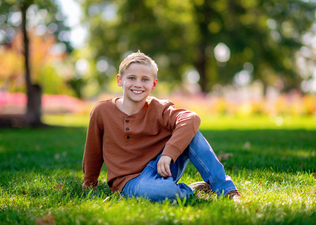 A boy in an orange shirt rests his elbow on his knee