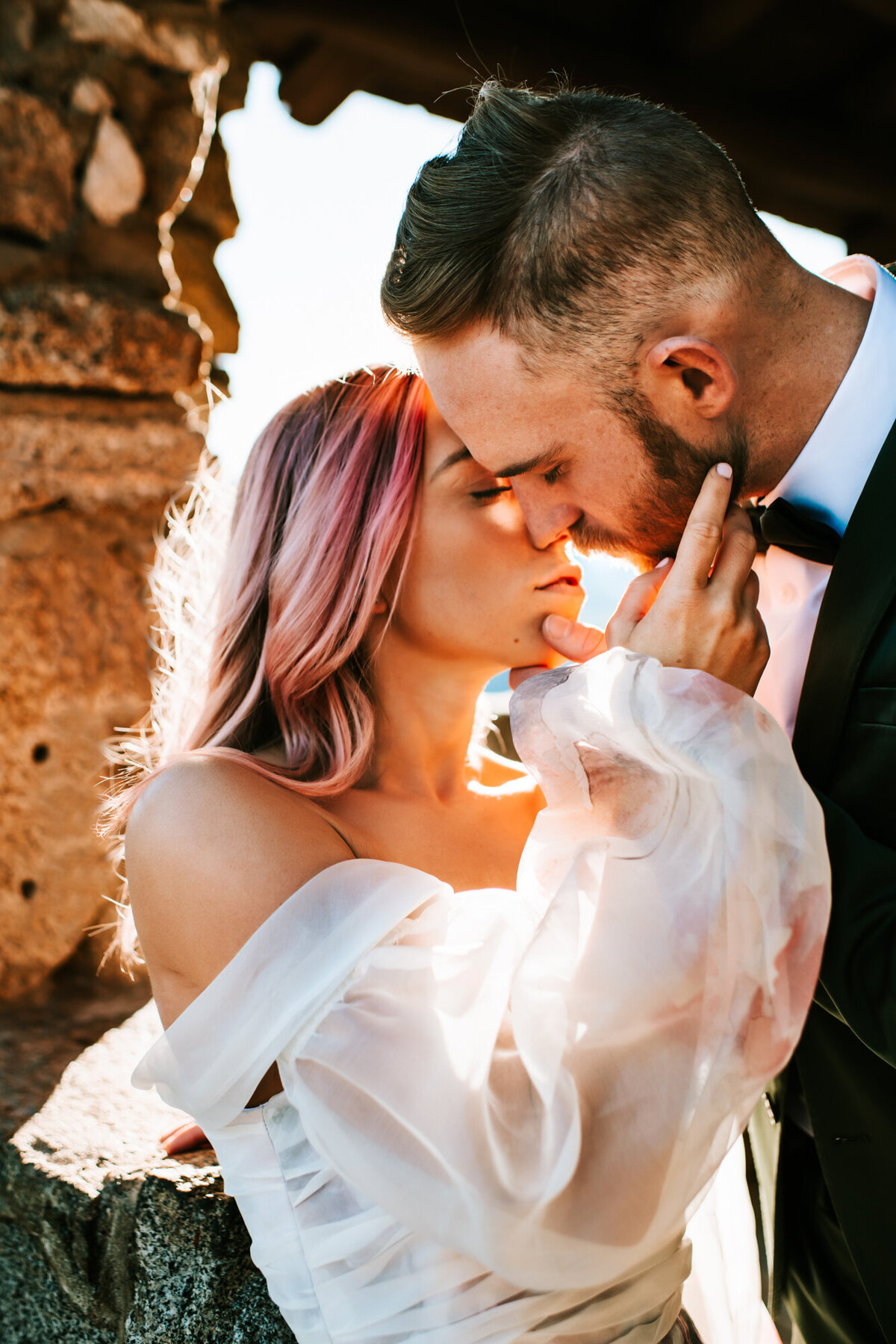 Couples Photography, woman in a wedding dress holds the face of a man in a suit who is leaning down and kissing her.