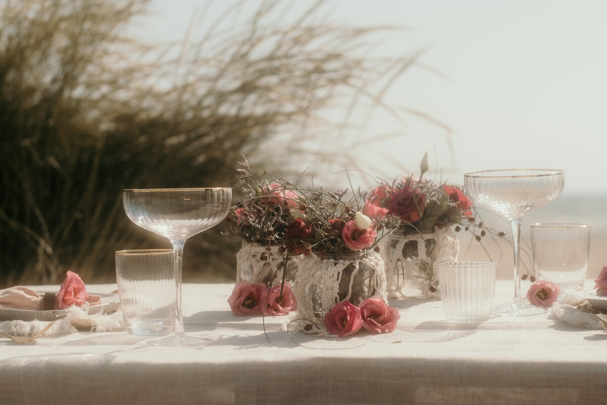 Drei Blumenvasen, Teller und Gläser stehen auf dem niedrigen Tisch am Strand bereit.