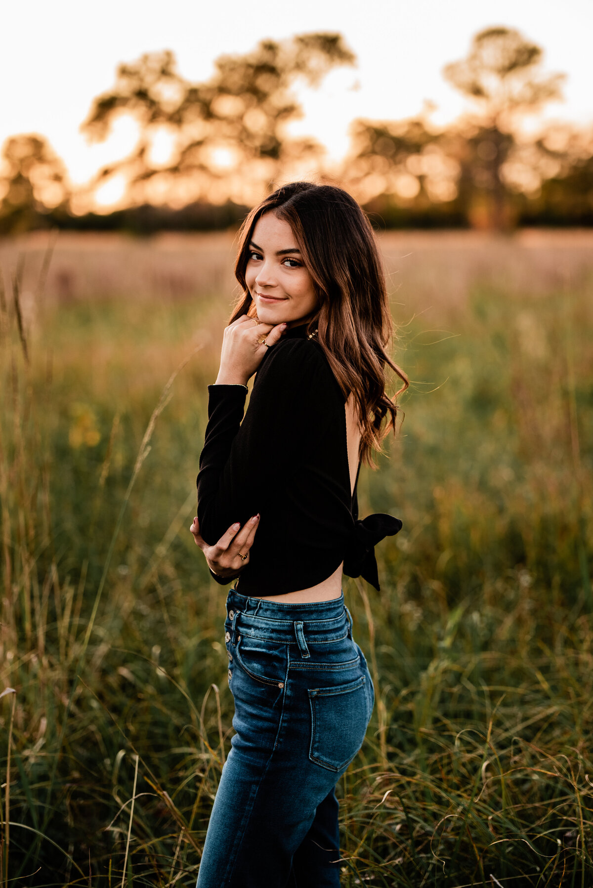 In an open field, a senior looks over her shoulder and smiles at the camera.