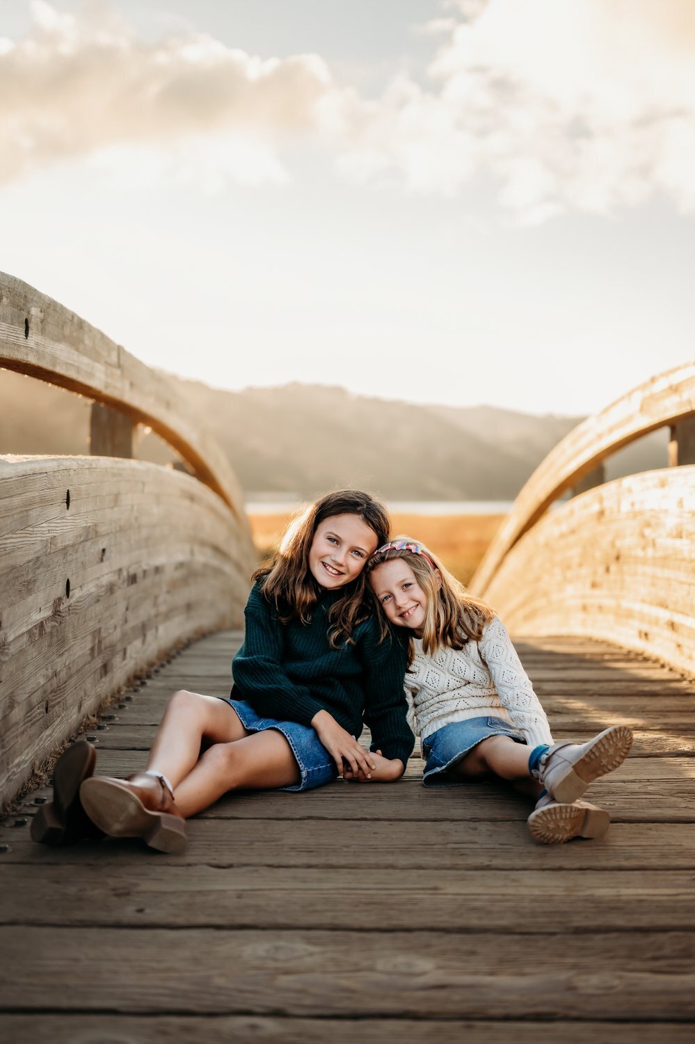 2 sisters sitting on the famous martinez bridge at grangers warf. the sun sets behind the mountains in the distance