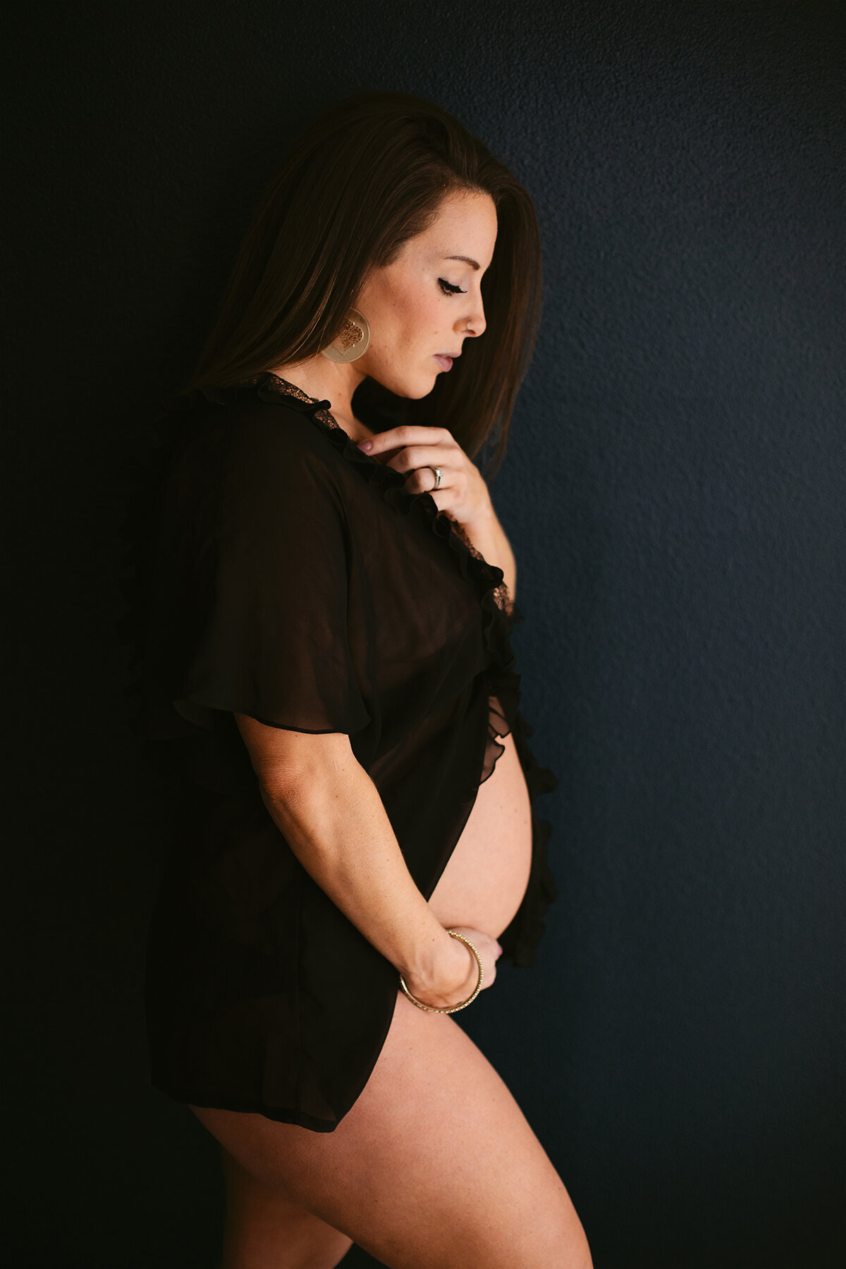 A woman looks down at her baby bump while wearing lingerie in during her Bentonville boudoir photoshoot.