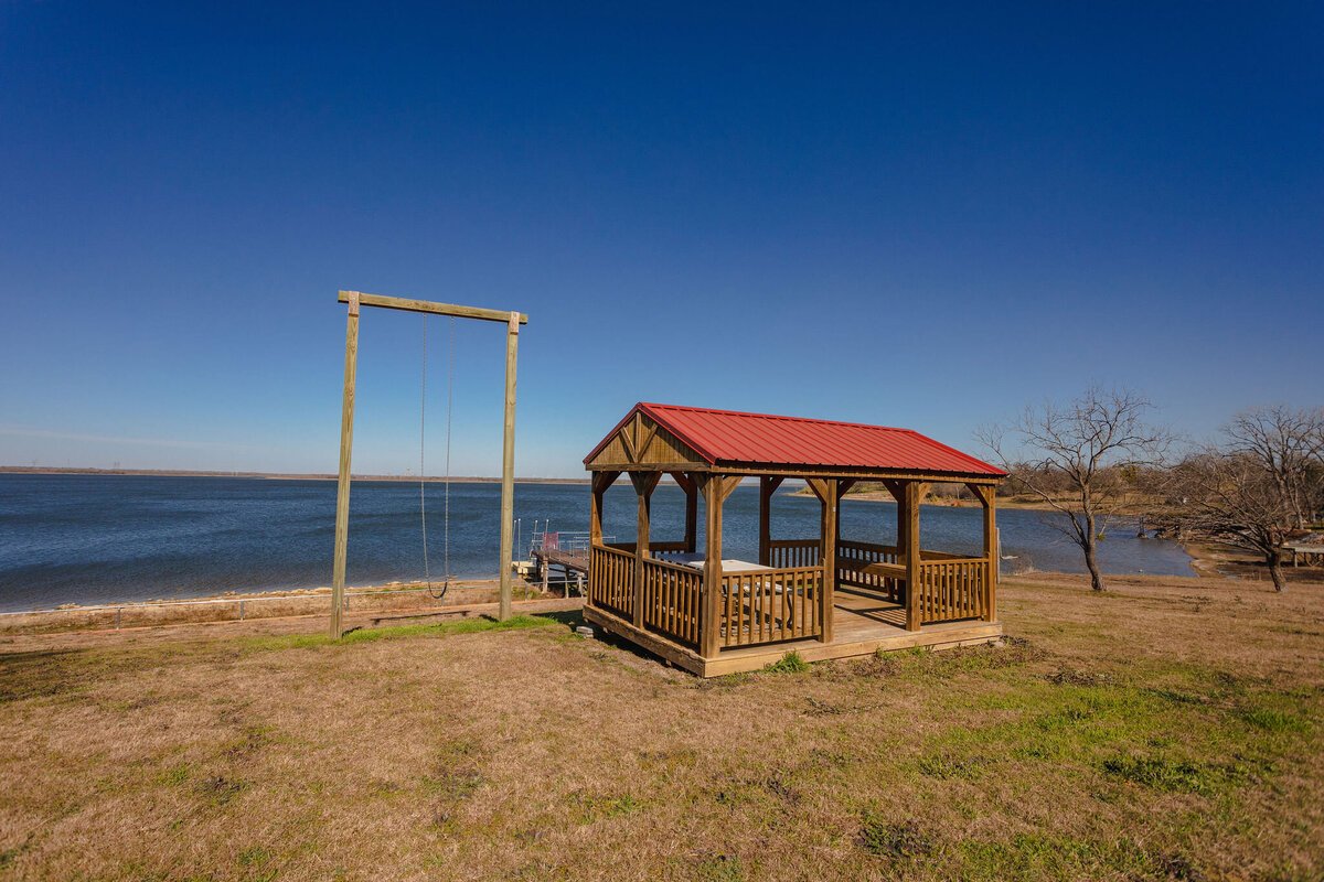 Covered outdoor patio with picnic table and swing at this 2-bedroom, 2-bathroom lakeside vacation rental home for 6 guests on Tradinghouse Lake with privacy access to a fishing dock and boat launch pad, ping pong table, gazebo, free wifi and free parking in Waco, TX.