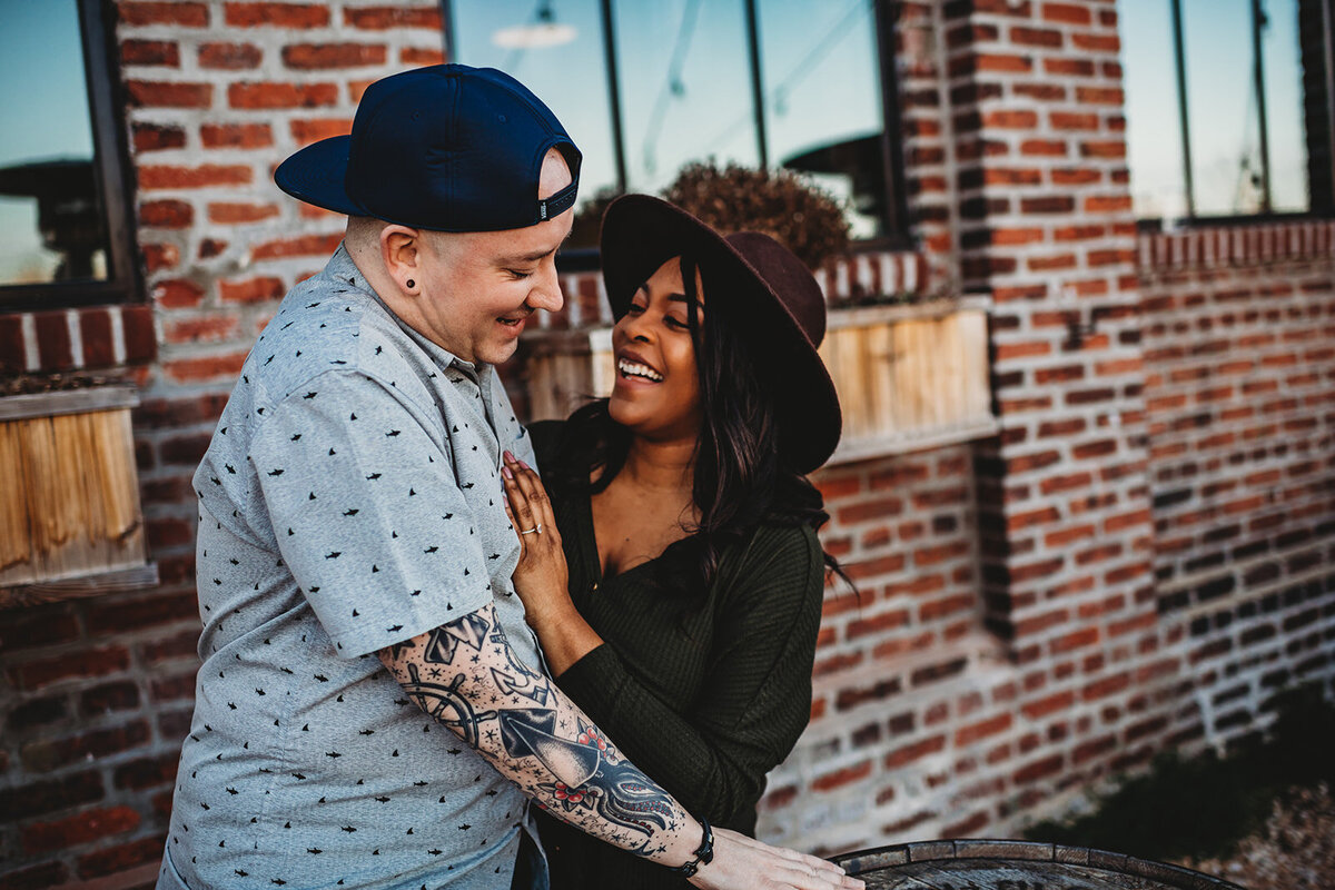 couples photography with man and woman embracing one another next to a red brick building for their engagement photos with Baltimore photographers
