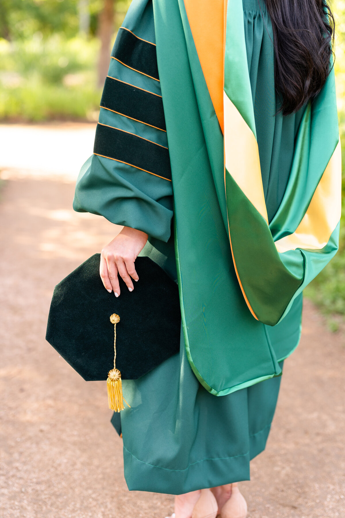 Baylor senior girl with close up of holding doctorate hat while wearing gown and hood at Houston Arboretum