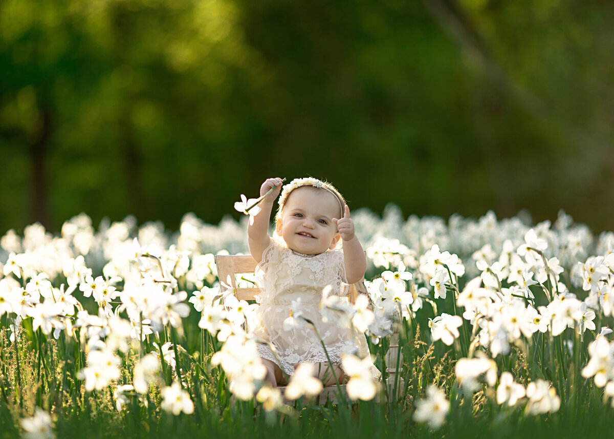 A toddler girl sits in a chair in the middle of a field of wildflowers while playing
