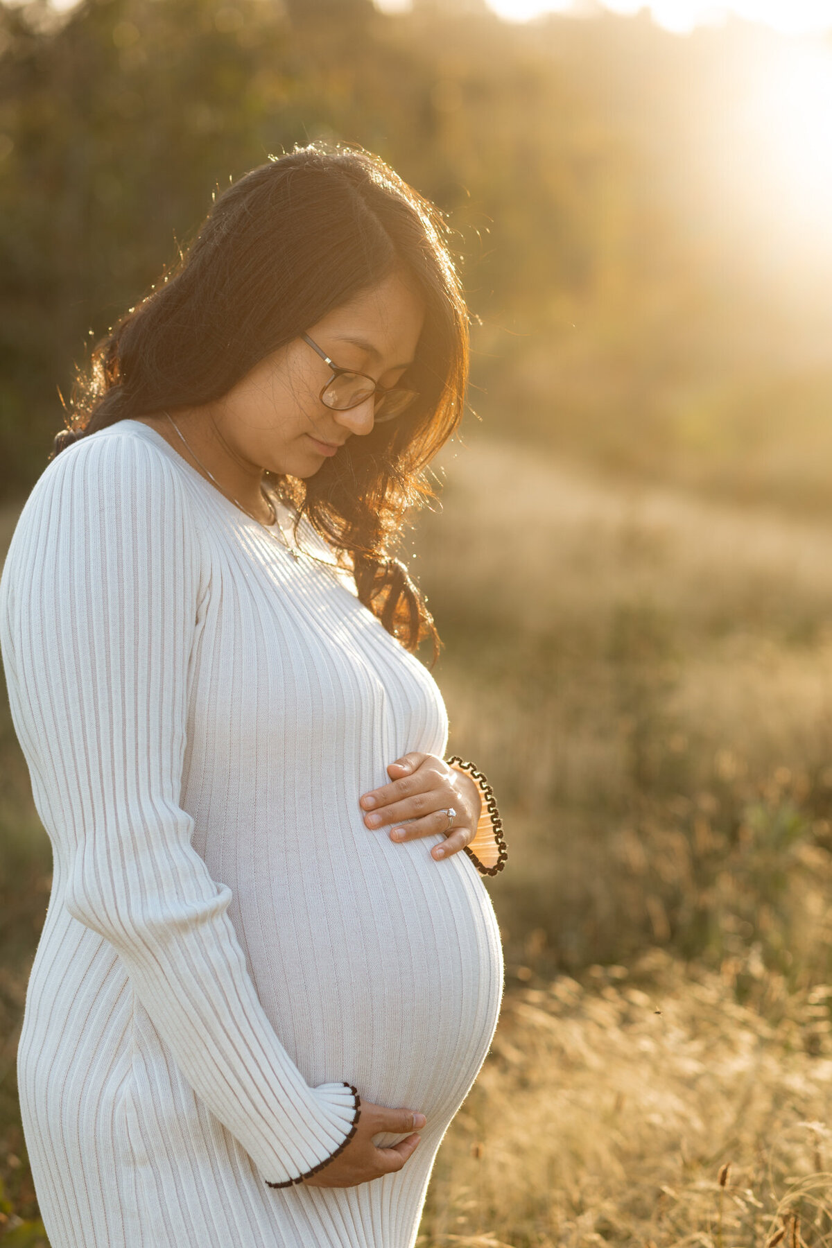 Pregnant woman in white dress standing in a sunlit field during a golden hour maternity photoshoot in Sydney