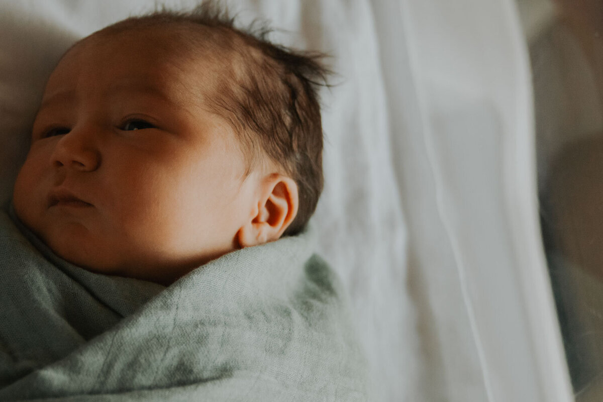 Close-up of a newborn wrapped in a green swaddle, gazing softly into the distance