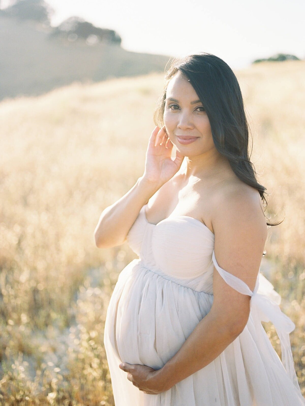 Hillside maternity photoshoot in San Francisco with a pregnant woman standing in a field against hills.