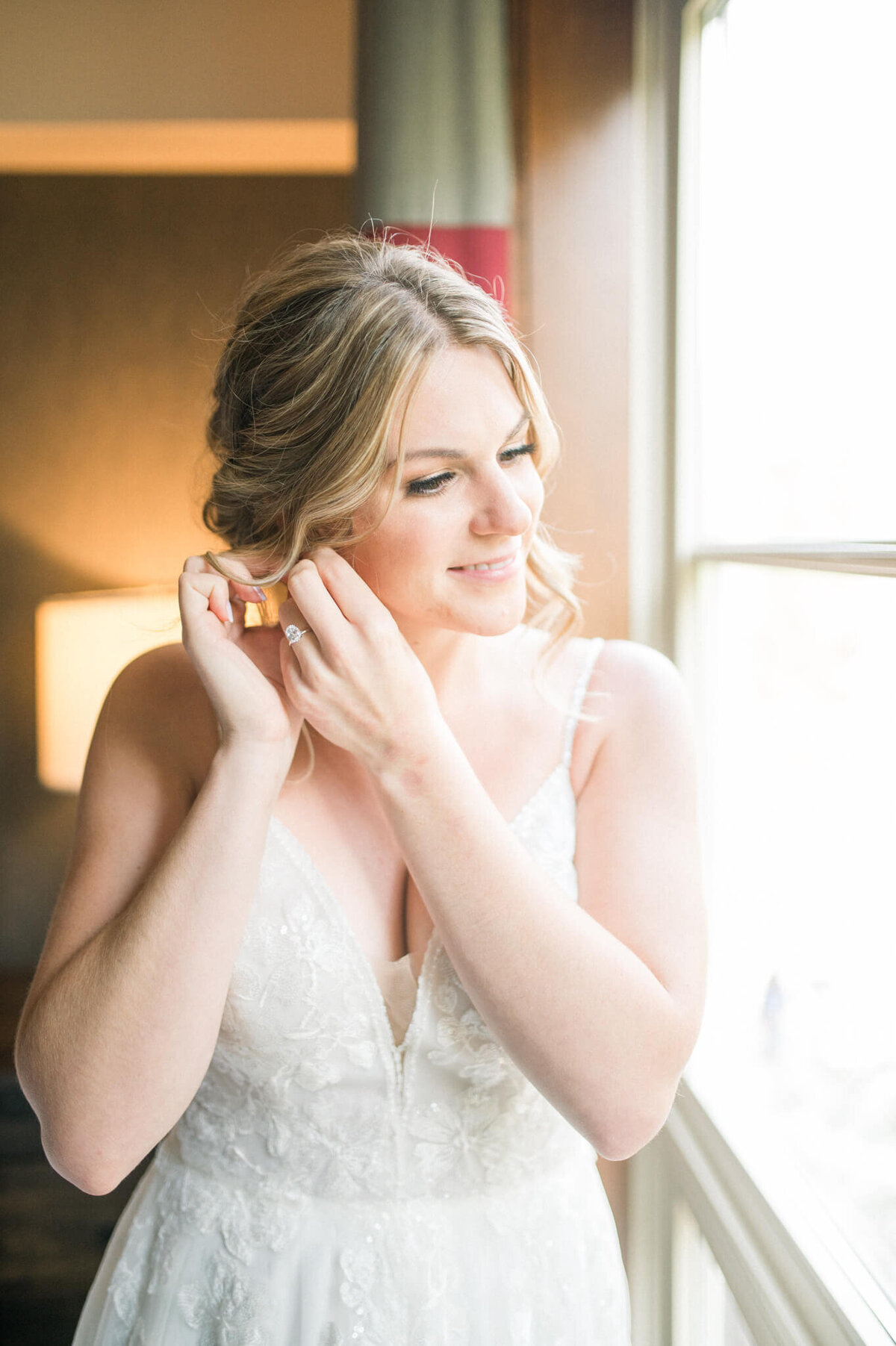 Bride putting on her earrings in front of the window