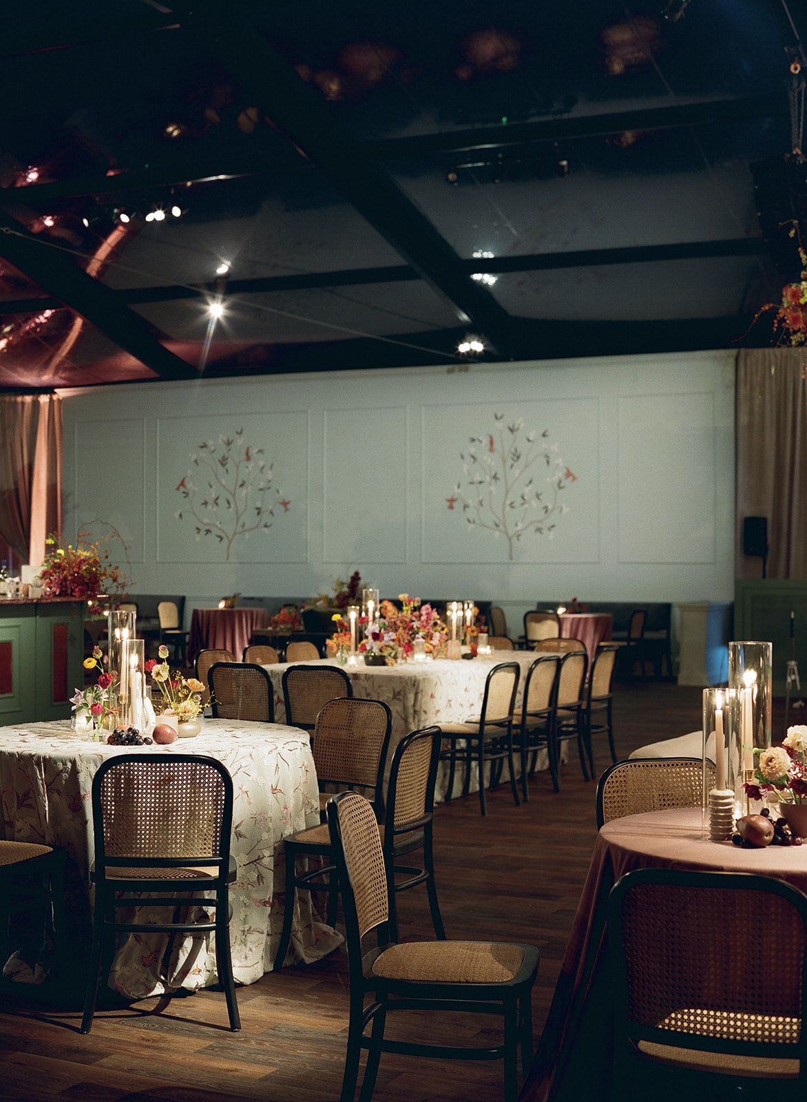 Clustered and styled floral arrangements, fruits, and art pieces for fall wedding reception. Low centerpieces mixed with ikebana arrangements and bud vases decorate the reception tables at this fall wedding. Floral centerpieces featuring orchids, ranunculus, sweet peas, and bittersweet. Styled wedding tables with fruits, curated candles, and floral arrangements. Tasteful fall color palette of copper, ruby, gold, burgundy, rust, and lavender. Design by Rosemary & Finch Floral Design in Nashville, TN.