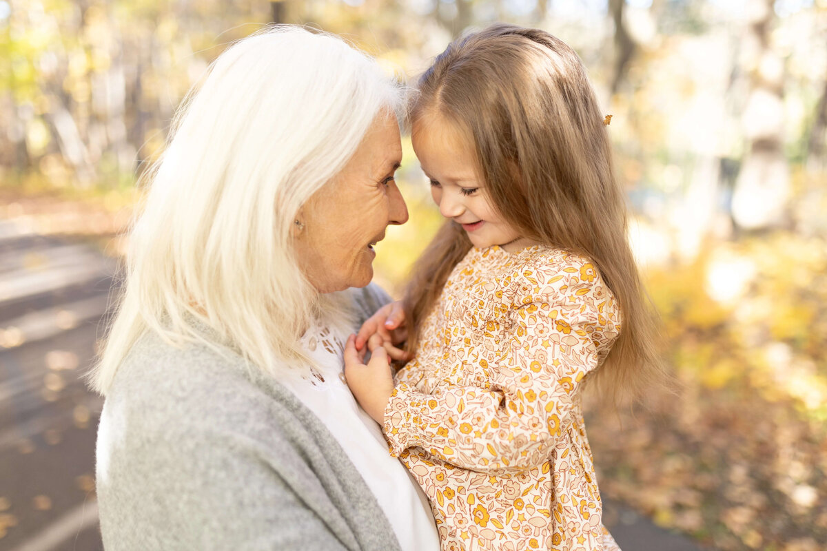 Grandma smiling forehead-to-forehead with granddaughter during fall session in Maple Grove