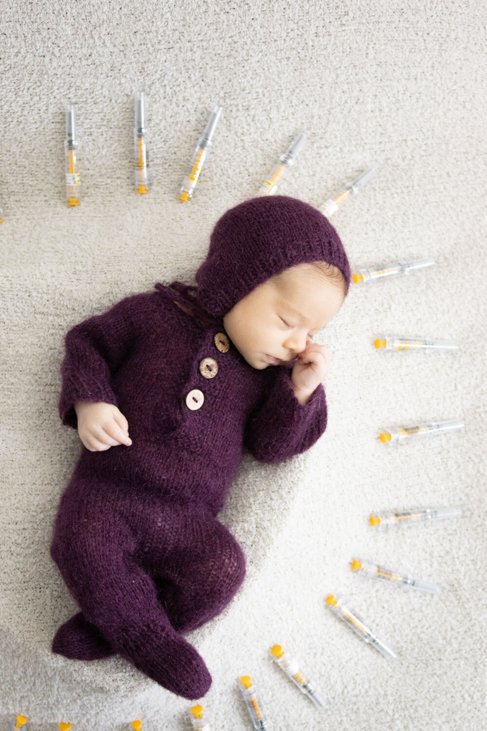 Baby in purple outfit, surrounded by syringes in a circle