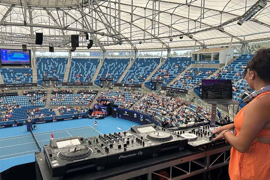 Female DJ playing a set overlooking a tennis match inside a packed United Cup stadium