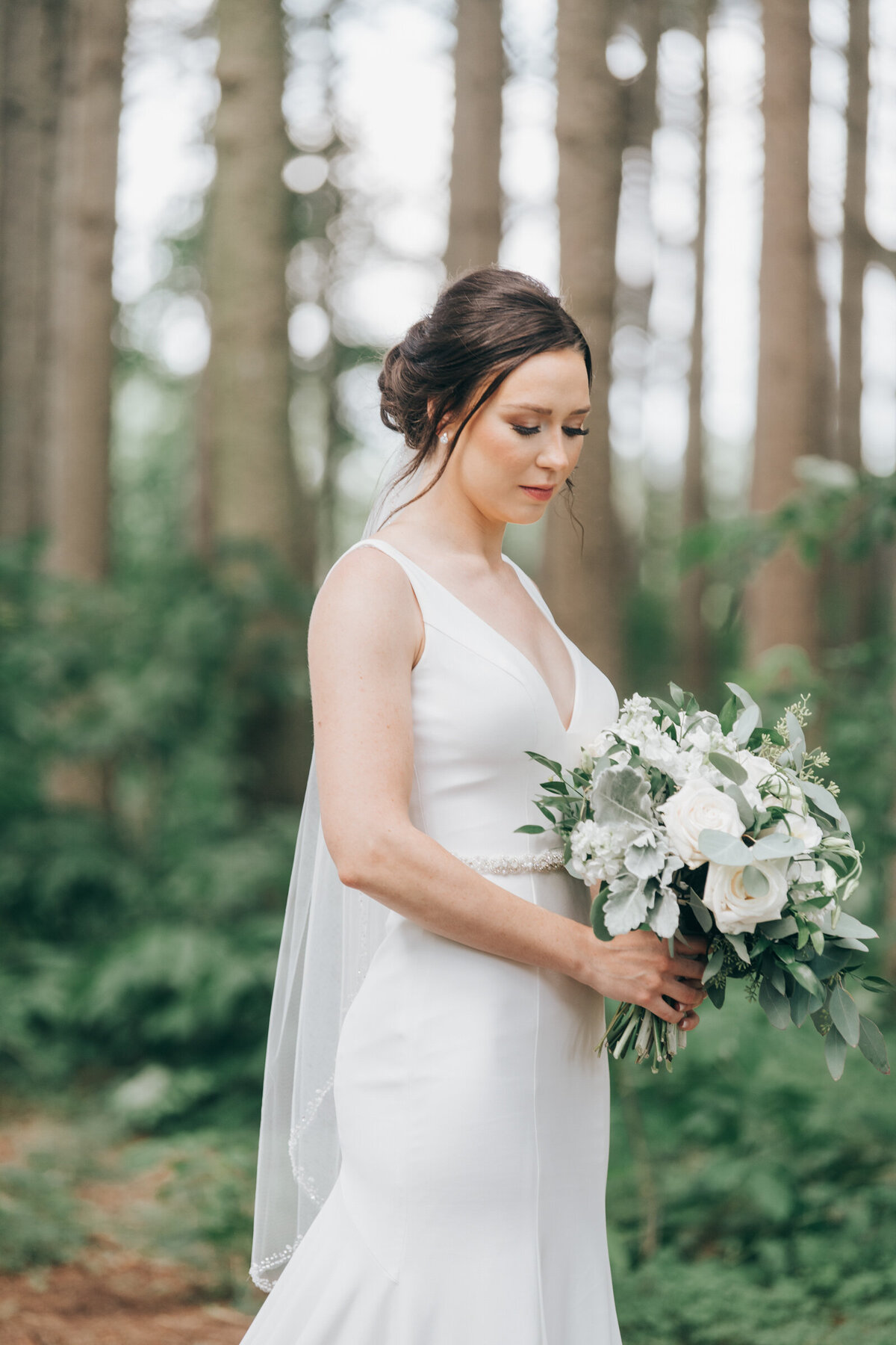 An elegant bride in a white dress looking at her beautiful wedding bouquet with white flowers