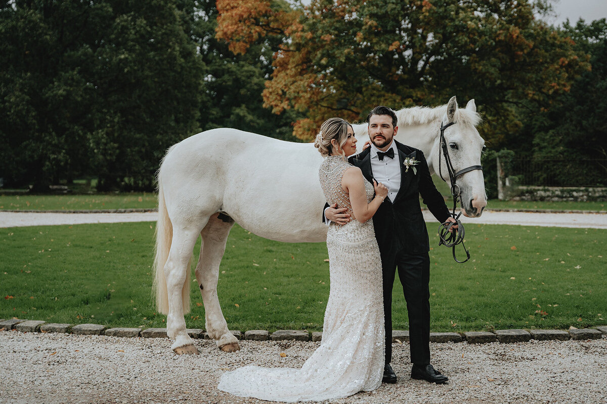 Bride looking at husband in front of white horse