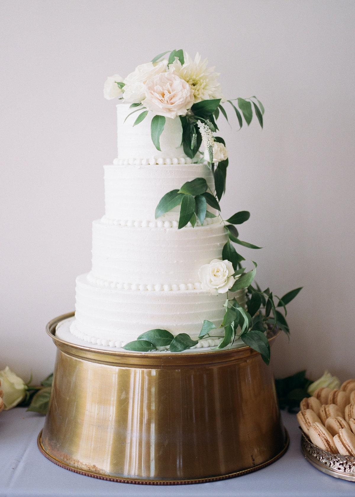 four tiered white wedding cake with greenery and roses