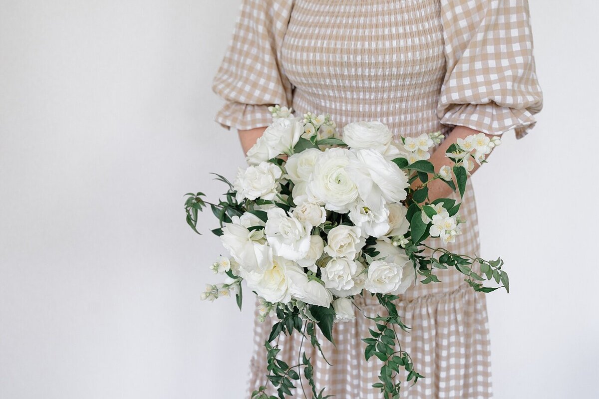 woman in a plain cream dress holding a white rose bouquet for branding photography