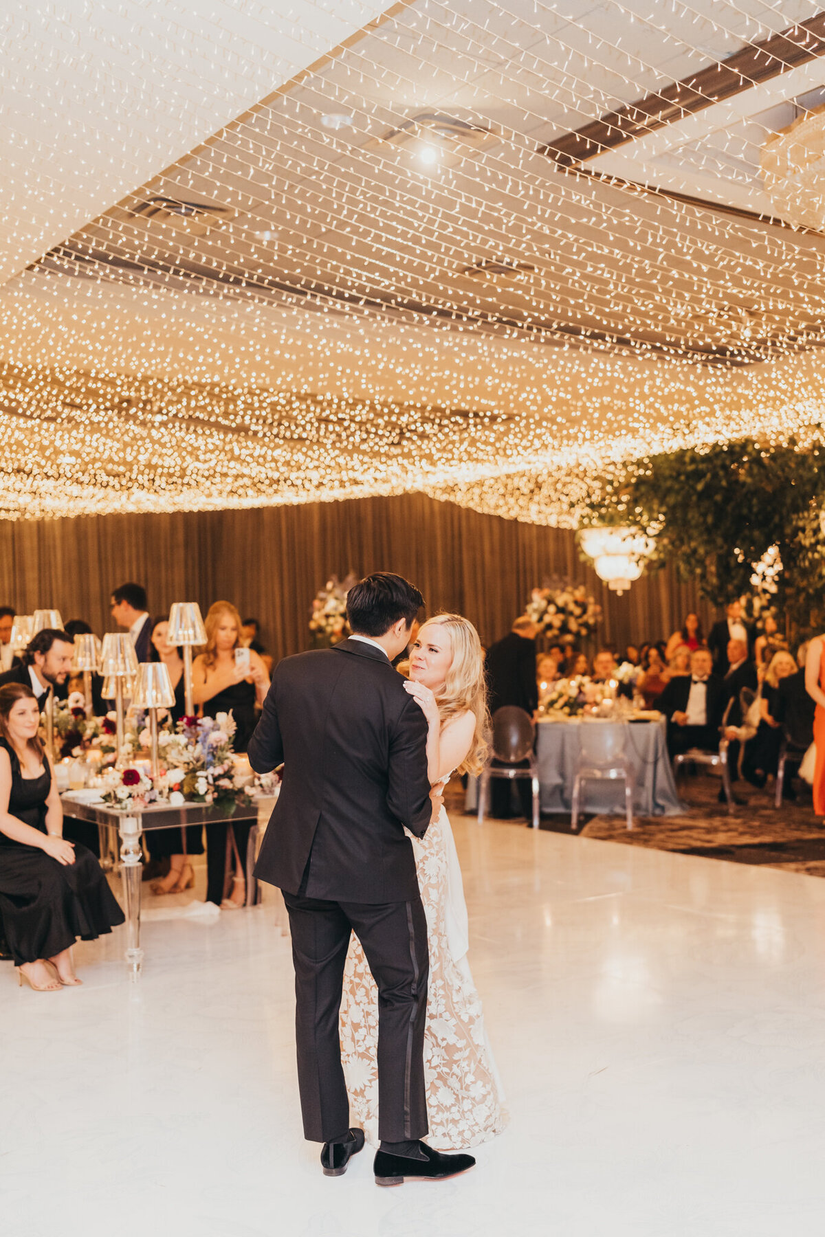 bride and groom share their first dance while friends and family watch