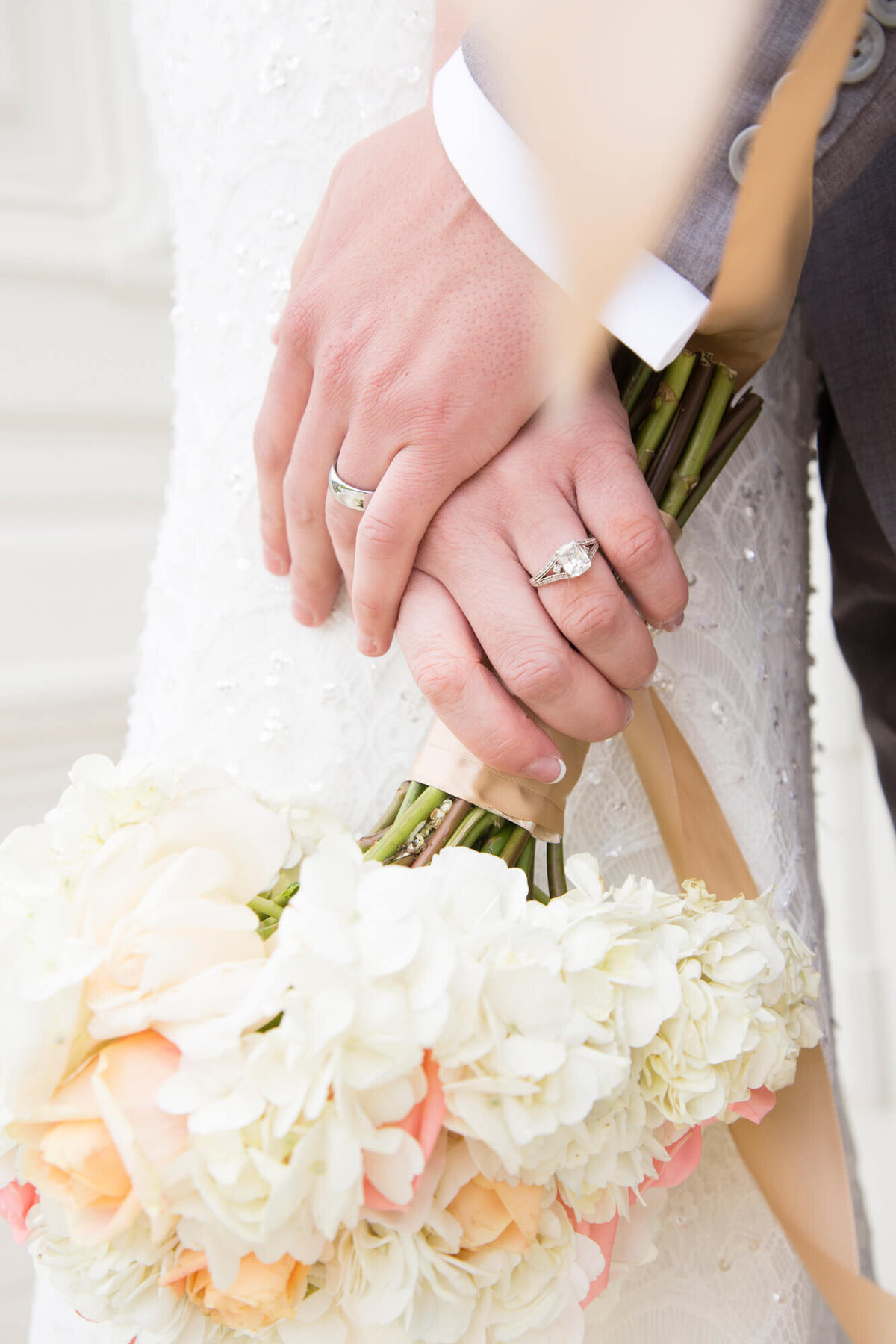 classic and bright wedding day detail of wedding bands while couple holds bridal bouquet