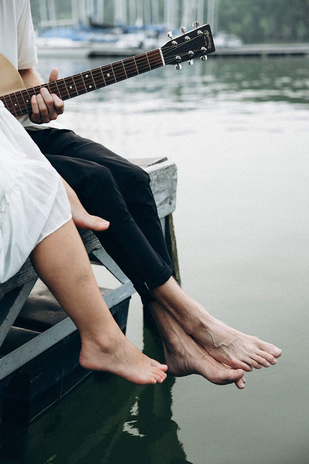 Feet hang romantically above the water off a dock over a lake.
