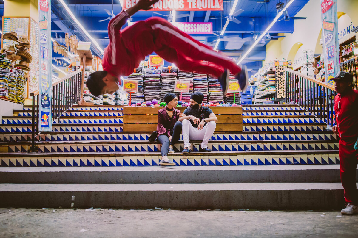 An engaged couple sitting on the steps talking while breakdancers do a flip in the foreground in downtown cancun mexico