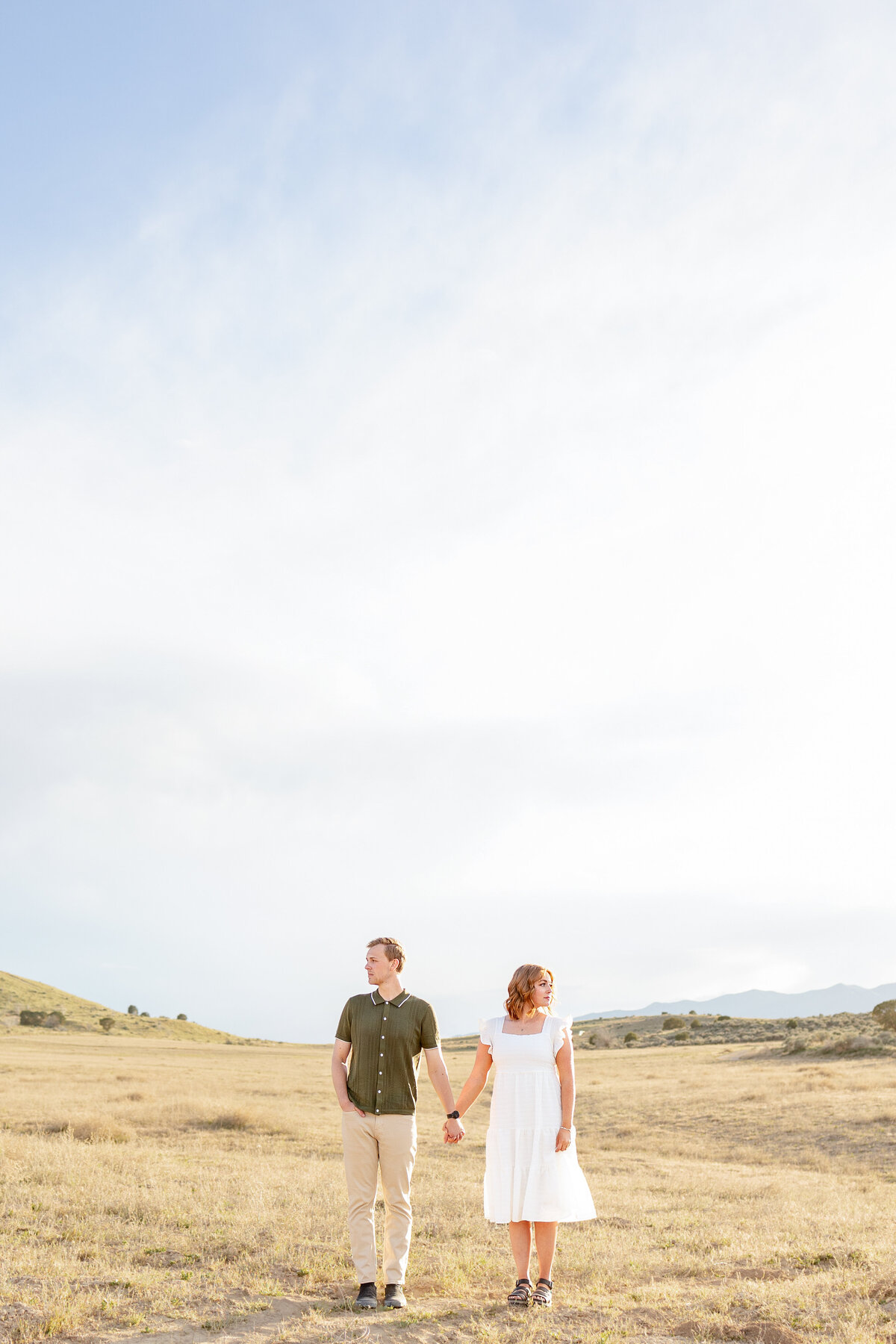 Future husband and wife holding hands while looking in opposite directions as they enjoy the desert views around them