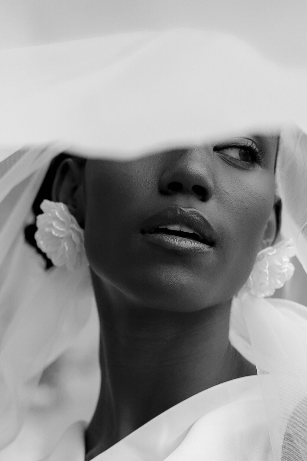 High-fashion bridal portrait in black and white: close-up of the bride's face with a flowing veil, showcasing the Vogue-like aesthetic of luxury wedding photography.
