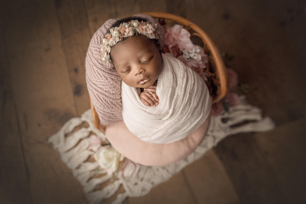 baby wrapped in light pink and placed on bamboo chair during newborn session in Hamilton