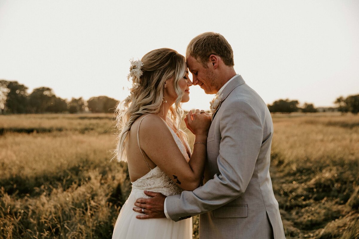Bride and groom facing each other with their heads together for rustic farm wedding photo during golden hour.