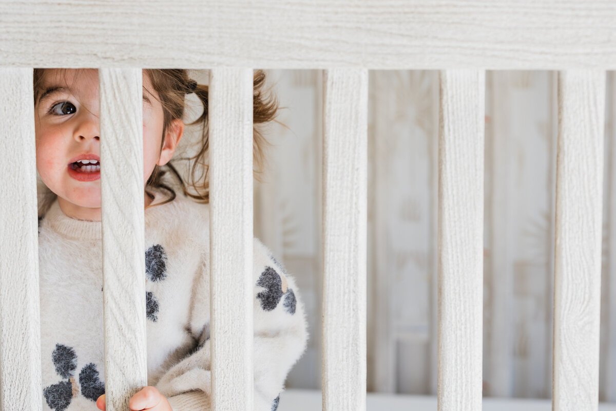 girl-looking-through-slats-of-crib