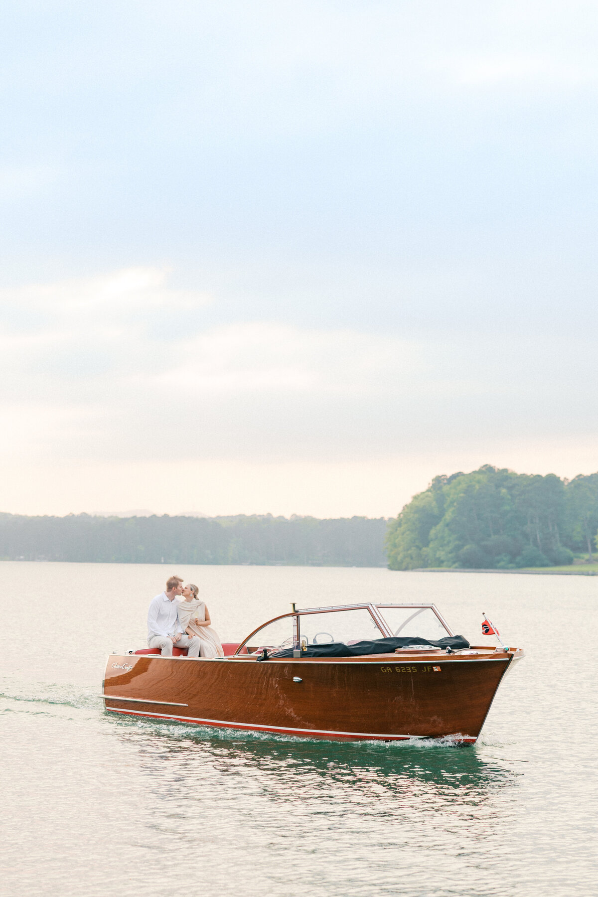 Couple kisses sitting on the back of their boat at their lake oconee engagement session