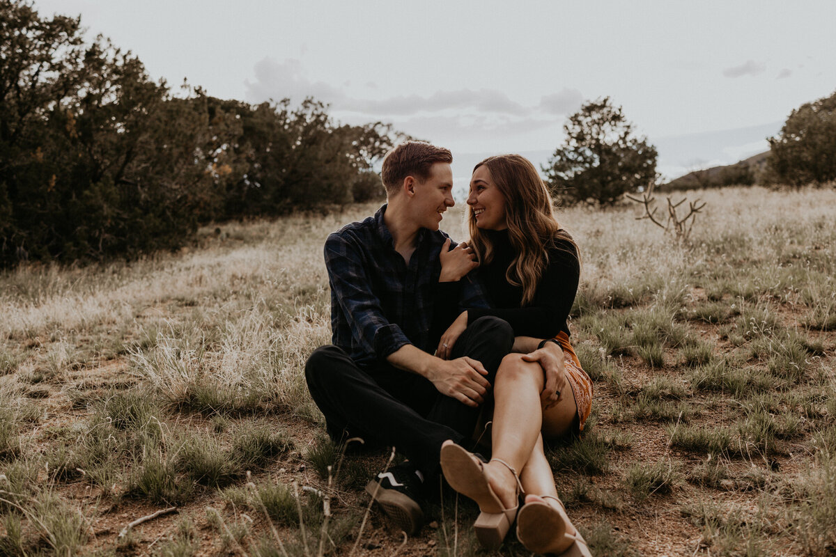man and woman sitting on the foothills of the Sandia mountains holding each other