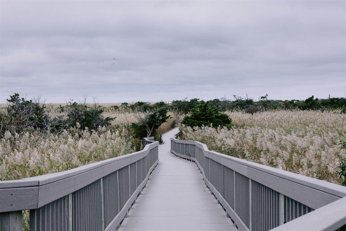 A long wooden bridge in the middle of a field at Fire Island Beach, NY. Engagement Image by Jenny Fu Studio